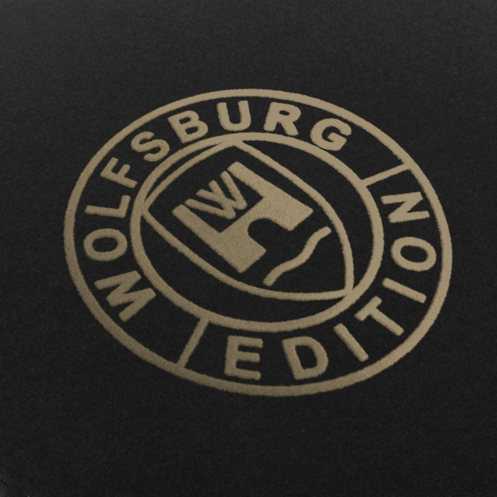 Das Wolfsburg Editions Logo auf einem schwarzen Teppich und das Logo ist in beige.