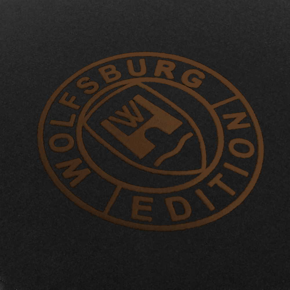 Das Wolfsburg Editions Logo auf einem schwarzen Teppich und das Logo ist in braun.